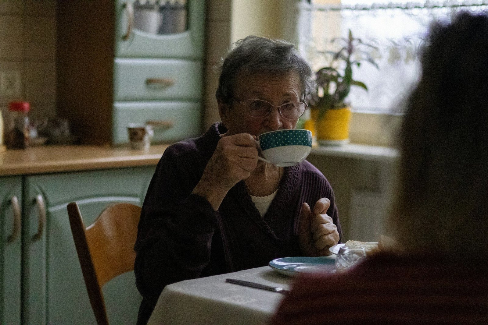 Een oudere vrouw drinkt koffie aan de keukentafel